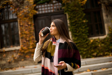 Fototapeta premium Young woman standing outside, drinking coffee to go and holding