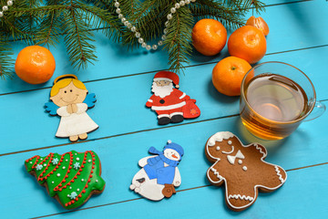 Handmade wooden Christmas tree decorations (Santa, Angel, penguin, rooster, Christmas tree, snowman) on a blue vintage table with Christmas tree and children's toys, tangerine, cakes. 