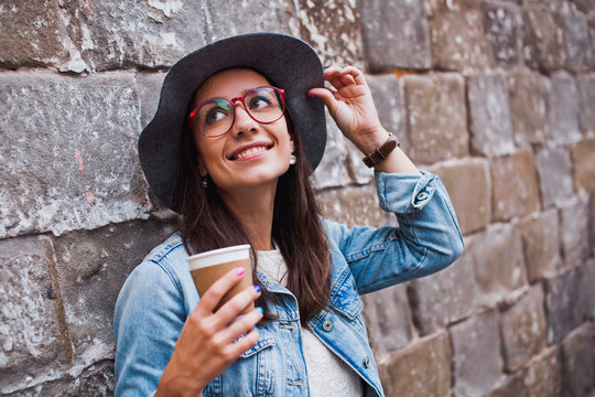 Hipster style woman wearing glasses and hat with coffee outdoors
