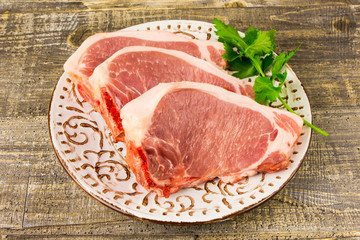 white plate raw sliced meat on wooden table, top view. Food, a knife, branches of greens