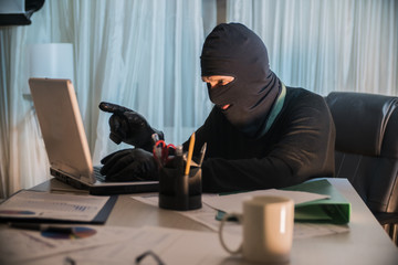 the thief hacker working on laptop in the night stealing data