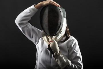 Front view portrait of woman wearing white fencing costume. She puts protective mask on her head.