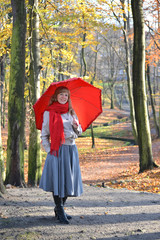 The young woman costs with a red umbrella in the autumn park