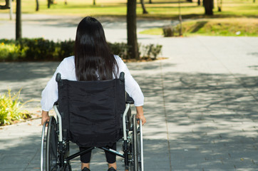 Young brunette woman sitting in wheelchair smiling with positive attitude, outdoors environment, physical recovery concept