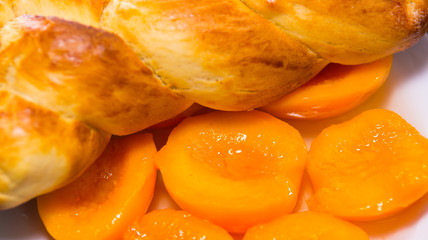 Closeup freshly baked sugar bread with beautiful golden color, white plate of sliced peaches, bakery concept