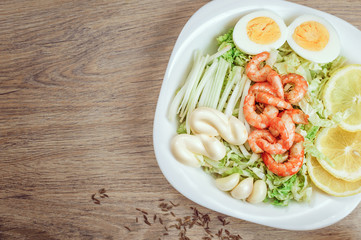 shrimp on lettuce with dressing, lemon, yaitsom, cloves of garlic in a bowl on a wooden background. Close-up