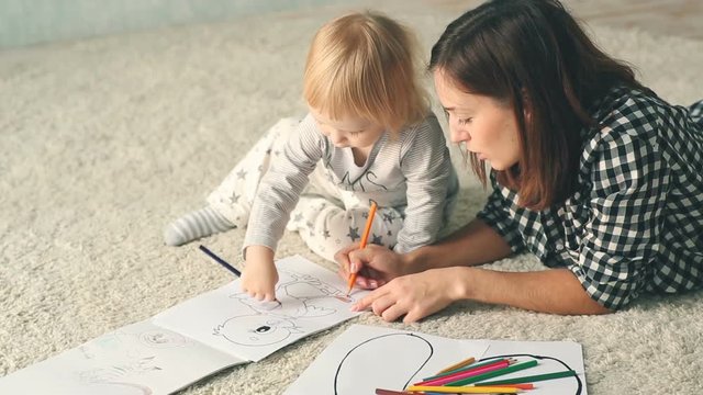 Mother with little daughter draws in album with pencils