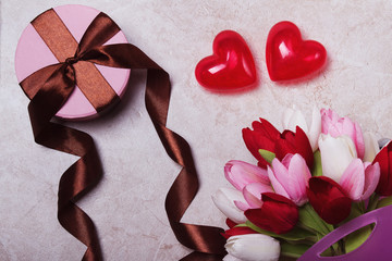 Round gift box with brown ribbons on a marble background. bouquet of tulip and two valentine's heart