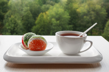 On the windowsill a Cup of tea and marmalade in a white ceramic dish. Breakfast on a green background. High key. Selective focus. For culinary publishers and websites.