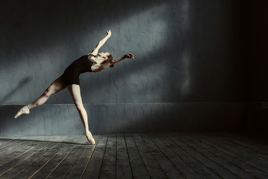 Skillful young ballet dancer acting in the black colored room