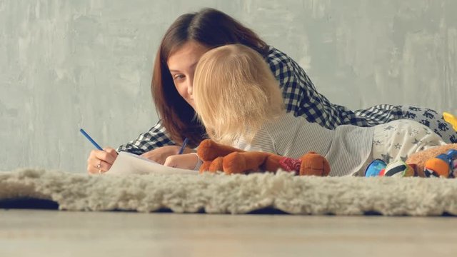 Mother and daughter girl draws a picture with pencils. Mother hugs and kisses baby.