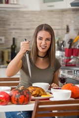 Portrait of a smiling young woman holding big kitchen knife ready to carve the holiday turkey.