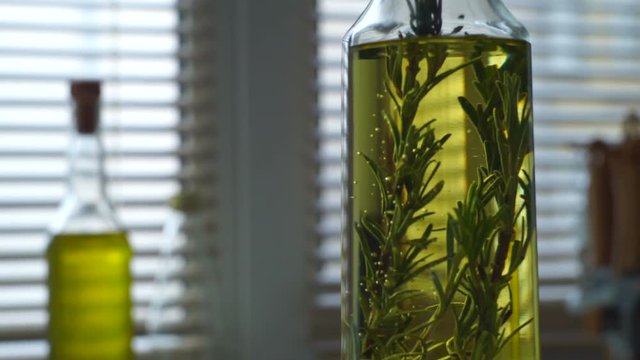 Olive oil with rosemary. Rosemary herb falls in olive oil bottle. Closeup of extra virgin olive oil in glass bottle at kitchen background. Italian food ingredient. Ingredient of greek food