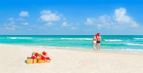Couple in Christmas Santa hats at beach with holiday gifts