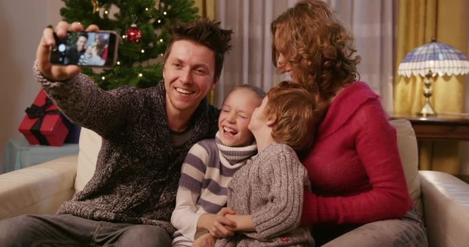 Loving Family Kissing Children Pulling Faces On Christmas Eve