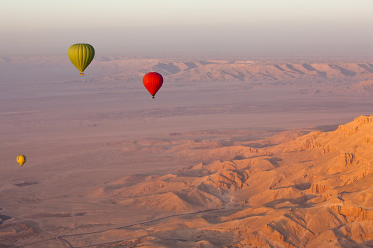 Hot air balloons suspended over the Theban hills of Luxor and the Valley of the Queens at sunrise, Thebes, Egypt