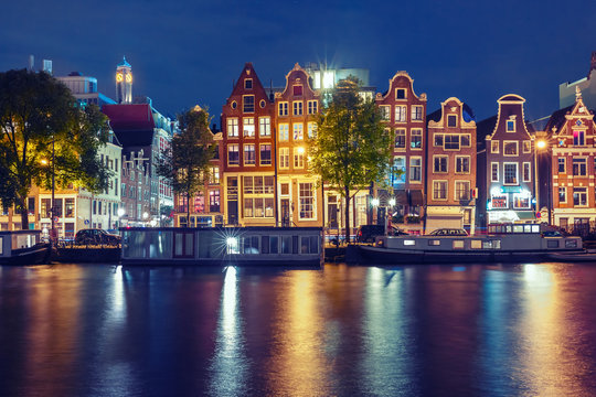 Amsterdam canal Amstel with typical dutch houses and houseboats with multi-colored reflections at night, Holland, Netherlands. Used toning