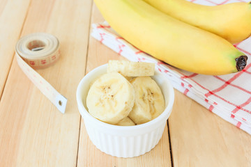 Two bananas and banana slices in white bowl with measuring tape on wooden table background, Concept of diet.