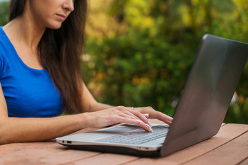 Close-up view of female hands on laptop keyboard. Student learning outdoors.
