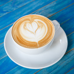Top view hot latte coffee in white cup on blue vintage wooden ta