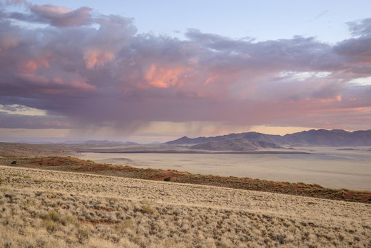 Some much needed rain falls in the distance at sunset in NamibRand Nature Reserve, Namib Desert, Namibia 