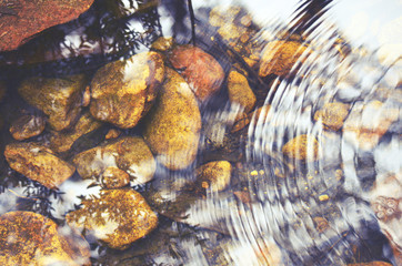 Concentric ripples and sky and tree reflections in a shallow pebble filled stream bed. Retro toned...