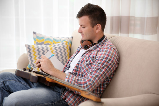 Young man with headphones composing music and sitting on the couch