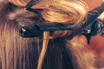 Stylist curling hair for young woman.