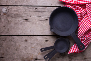 Empty frying pans on aged wooden background.