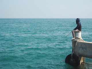 Unidentified man fishing using a rod from ocean/sea in Thailand.