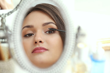 Obraz na płótnie Canvas Beautiful girl applying cosmetics in front of mirror