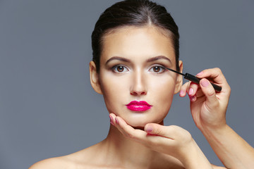 Beautiful girl applying cosmetics on grey background