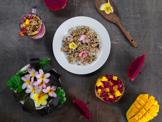Overhead still life of granola, colorful smoothie in glass jar and tropical fruits on dark shabby background,