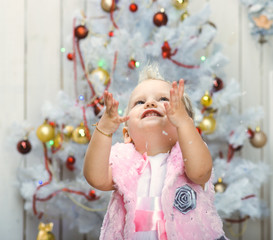 Little child standing near new-year-tree and catch snowflakes