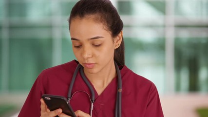 A medical professional uses her smart phone outside the hospital. A doctor uses her mobile phone outside her office. - Powered by Adobe