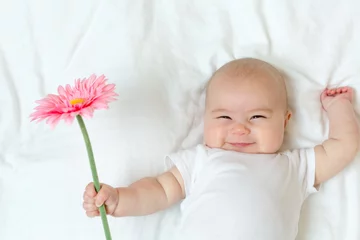 Fototapeten Happy newborn baby girl playing with a flower © Tierney