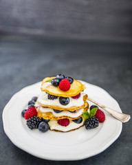 Delicious homemade pancakes with fresh ripe berries served on white plate on stone background.
