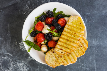Top view of fruit salad with mozzarella and toast on dark stone background.