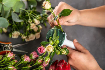 Female hands making beautiful bouquet of flowers on dark background