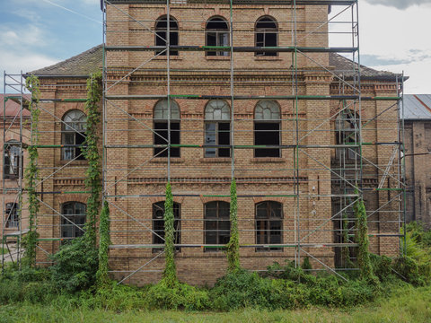 Picture of an old abandoned mansion-house with wooden trestle for alteration work. Verdurous mansion against the background of cloudy sky. Old mansion made of brown bricks.