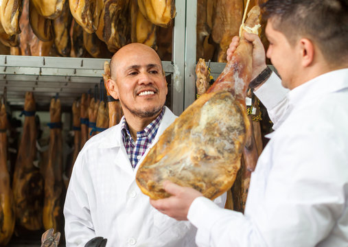 experienced technologist with butcher checking drying wurst and jamon at factory