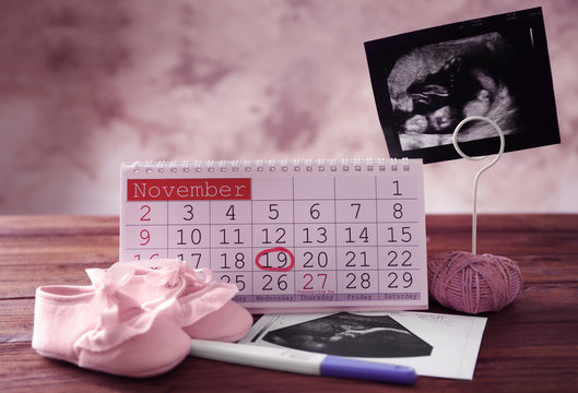 Calendar with mark, ultrasound picture of baby and children shoes on table