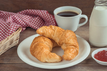 Croissants on plate with coffee cup, milk bottle and fruit jam