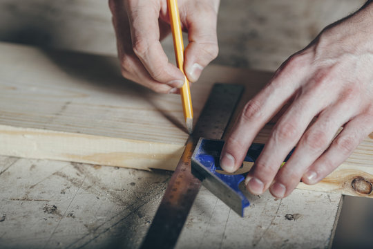 Cropped hands of carpenter marking on plank with pencil and ruler at workshop