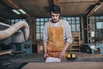 Carpenter reading document on bench in workshop