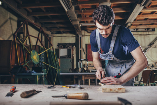 Carpenter using chisel on plank of wood in workshop
