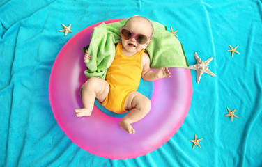 Cute baby with swimming ring, towel and sunglasses lying on blue bedspread. Holidays at sea with baby, concept