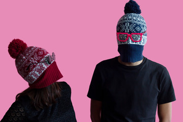 Young hipster couple fashion portrait; Wearing christmas hats as robber masks with bright glasses. Millennial idea of costume creative party in tumbler crazy style on abstract minimal pink background.