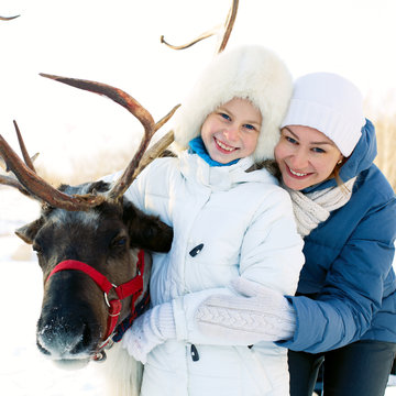Happy little girl with mom hugging her reindeer. Winter playtime