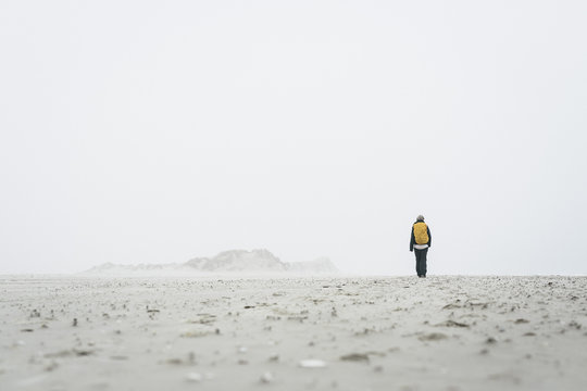 Rear view of female hiker walking on field against sky in foggy weather